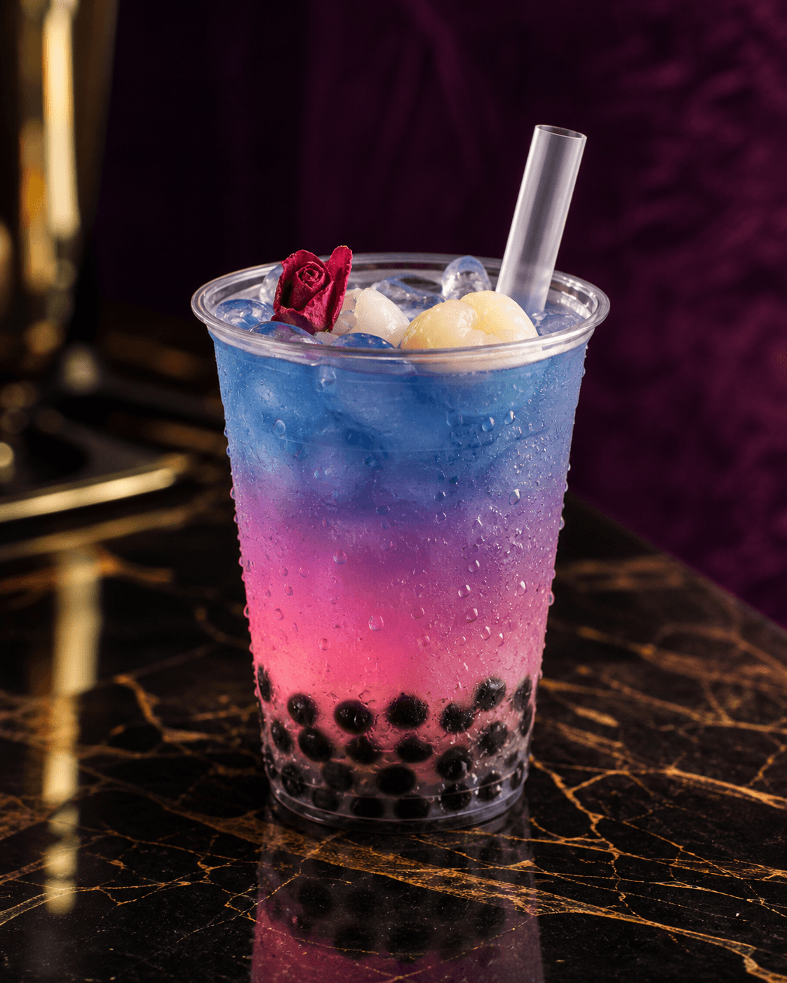 Lychee rose butterfly pea tea, layered blue into pink over black tapioca pearls, finished with a dried rose